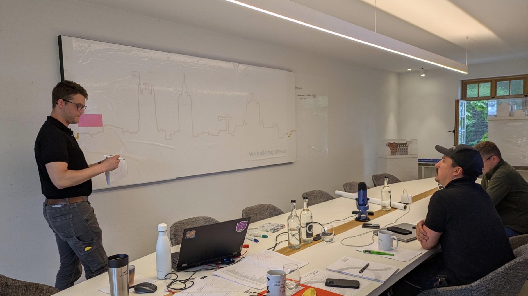 Sessie in een vergaderzaal, iemand schrijft op een whiteboard met een skyline.
