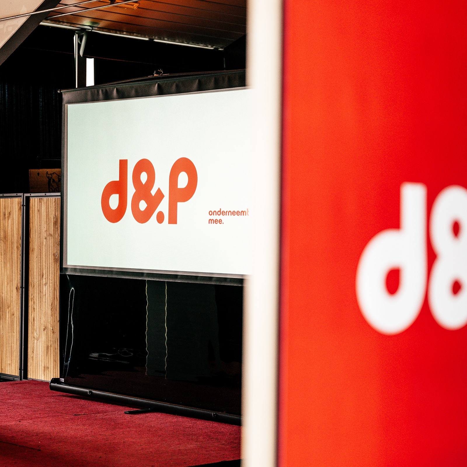 Projectiescherm met het logo van d en P naast een rode banner.