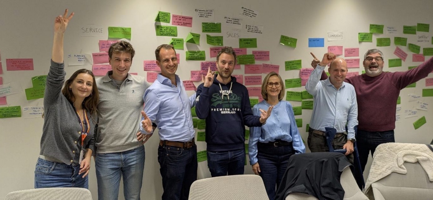 Zeven mensen voor een wand vol post-its, handen in de lucht.