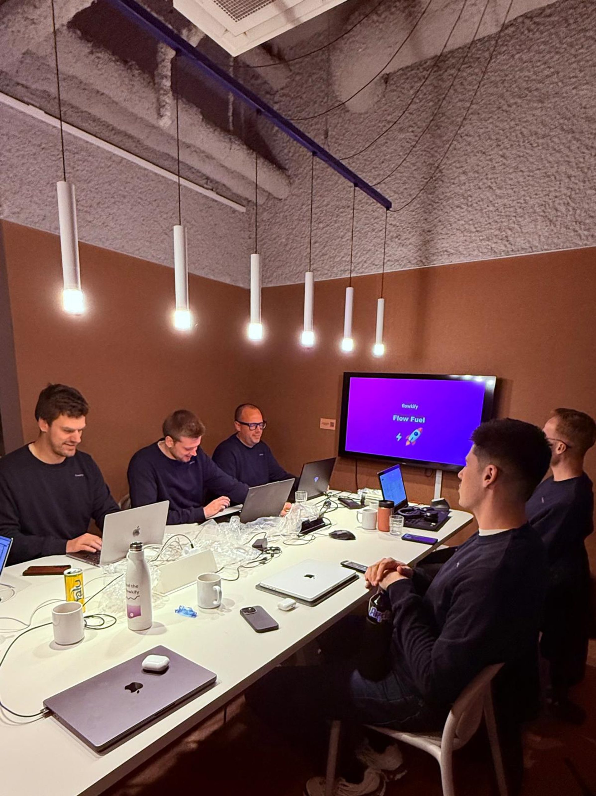 Het Flowkify-team werkt samen aan laptops rond de vergadertafel op kantoor.